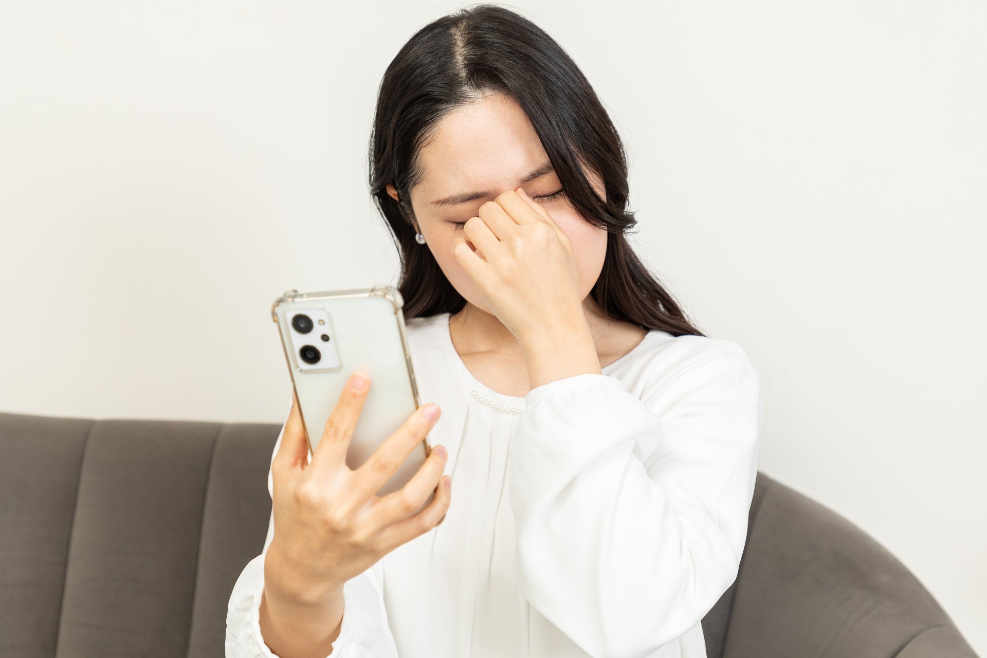 スマホを持ち目元を押さえる女性