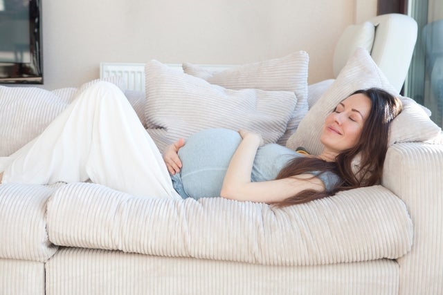 お腹を抱えながらベッドに横たわる妊婦さん