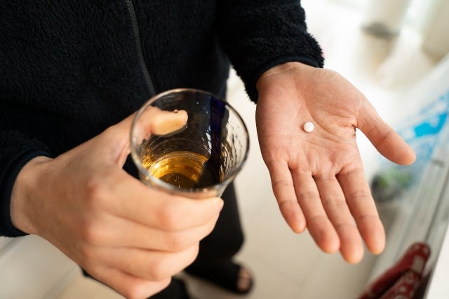 錠剤1粒と水の入ったコップを持つ男性