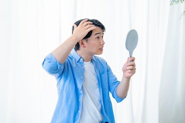 鏡を見ながら毛髪を気にする若い男性