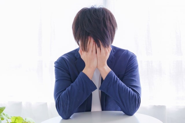 窓辺のテーブルに座り顔を両手で覆う男性