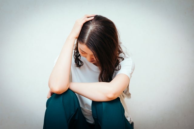 膝をかかえて落ち込んでいる女性のイメージ写真
