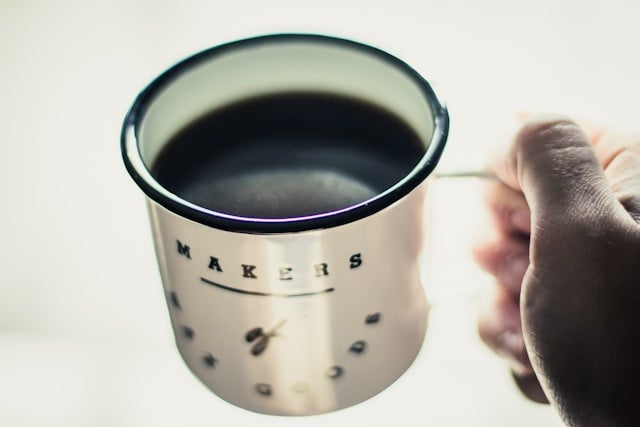 右手に持ったコーヒー入りのマグカップ