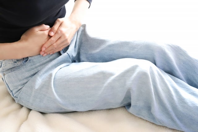 座位で腹部を両手で押さえる女性
