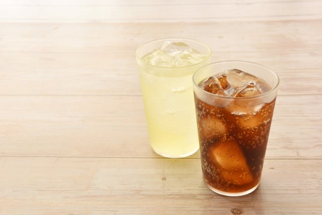 木目のテーブルに置かれたコップ入りの2種類の炭酸飲料