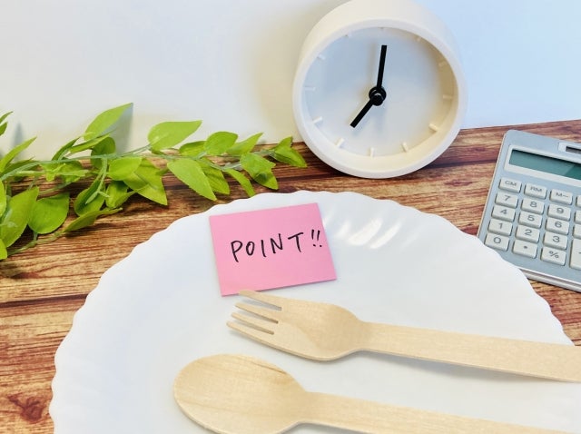 白い皿の上のスプーンとフォークとPOINTと書かれた付箋、卓上時計、電卓
