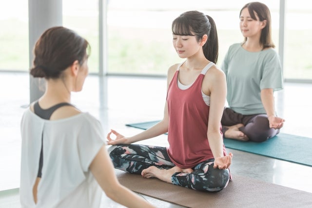 目を瞑ってヨガをしている３人の女性