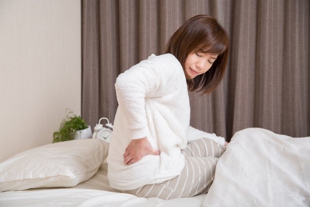 ベットの上で腰を押さえいる女性