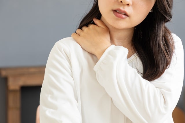 自分の右肩に左手を乗せる女性