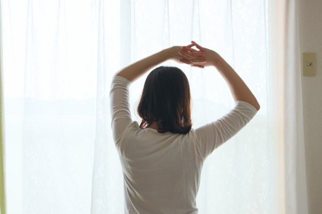 窓の前で両手を上げる女性の後ろ姿
