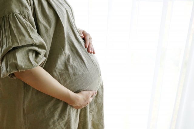 大きいお腹に手を添えるワンピース姿の妊婦さん
