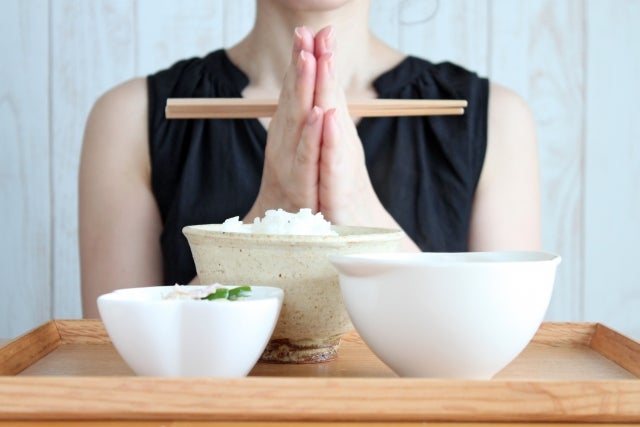 食事を前に箸を持ち手を合わせる女性