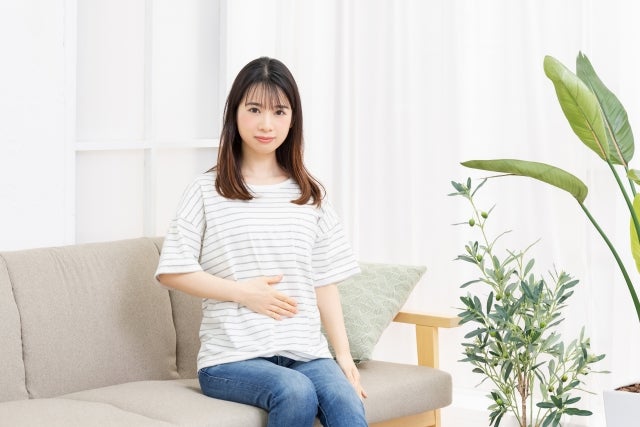 お腹に手を当ててソファに座る女性の写真