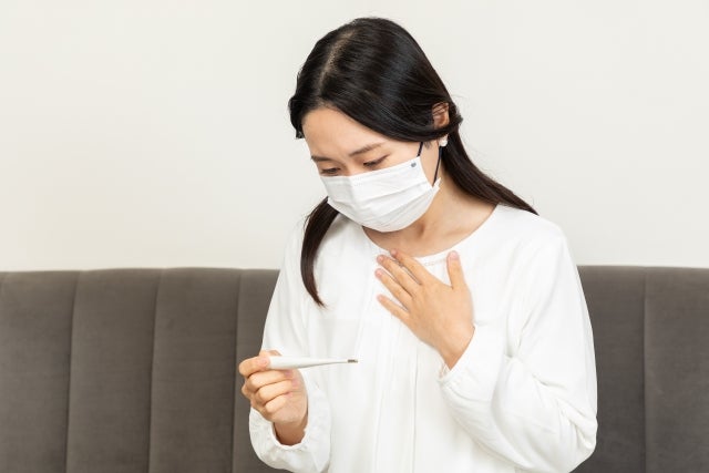 マスクをして手に持った体温計をみている女性
