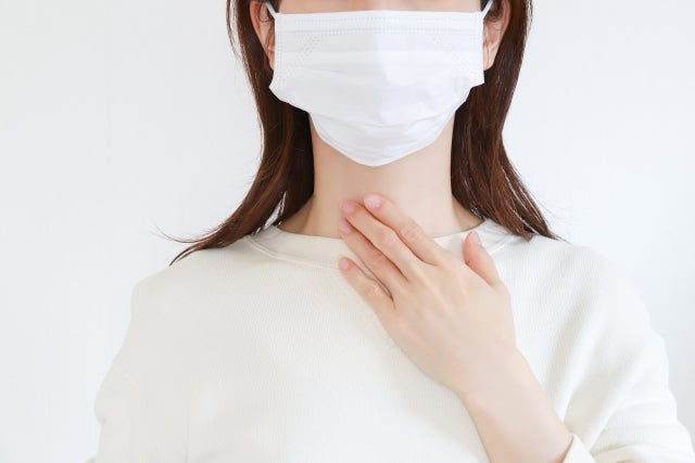マスクをして喉のあたりに手を当てている女性