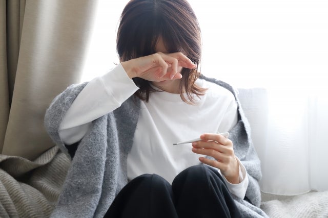 額に手を当て体温計を持つ女性