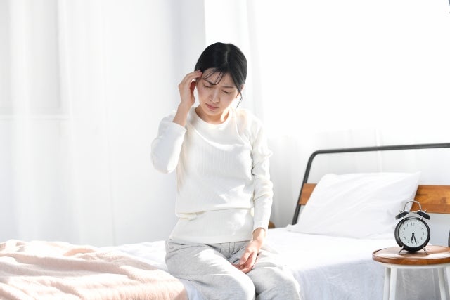 ベッドに座りこめかみに手を当てる女性