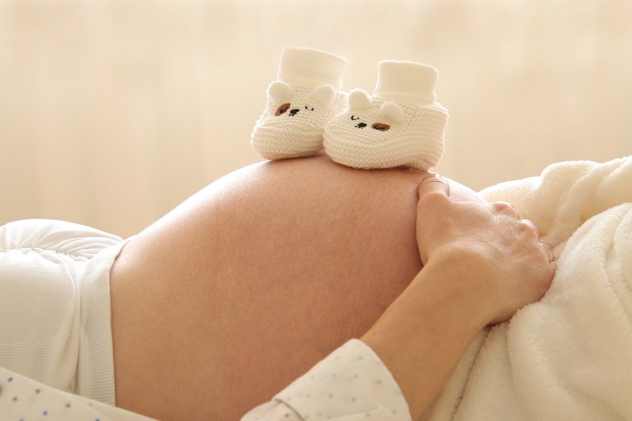 妊婦さんのお腹の上に赤ちゃん用の靴が置かれています