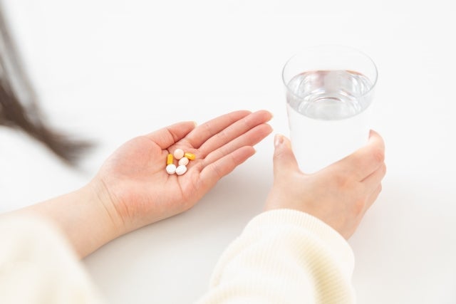 手に錠剤と水の入ったコップを持つ人