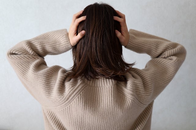 両手であたまを押さえている女性の後ろ姿
