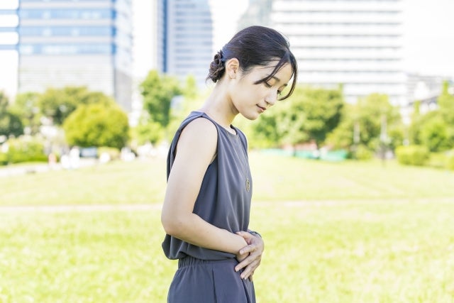 腹部を押さえ気分が悪そうにする女性