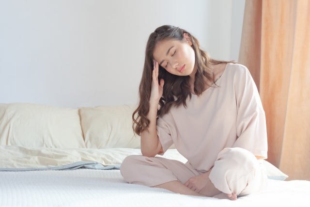 ベッドの上に座り頭を押さえる女性